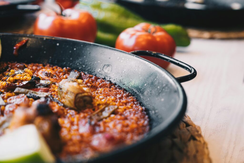 Close-up of a flavorful paella dish in a pan with fresh tomatoes and greens.